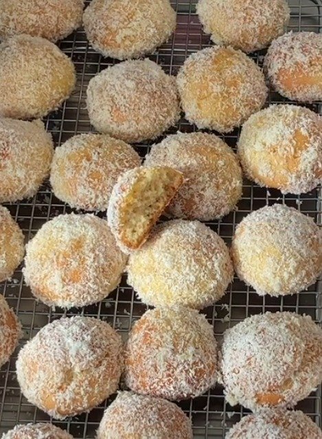 Photo de petits gâteaux ronds à la noix de coco, dorés et parsemés de copeaux de coco sur une plaque de cuisson.