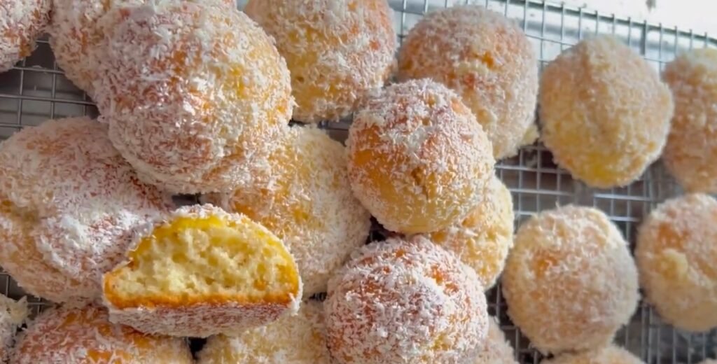 Photo de petits gâteaux ronds à la noix de coco, dorés et parsemés de copeaux de coco sur une plaque de cuisson.