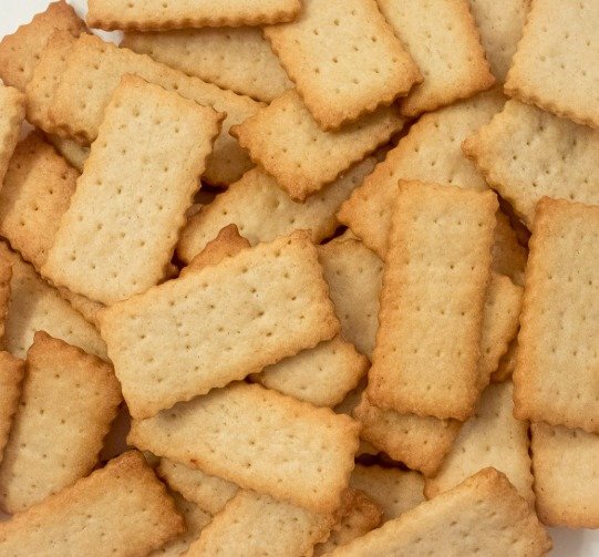 Biscuits dorés aux bords dentelés disposés sur une grille à pâtisserie, saupoudrés de sucre fin.