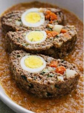 Photo d'un rouleau de viande hachée tranché, montrant une texture juteuse, servi avec une sauce tomate et du persil.