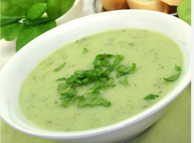 Bol de soupe d'un vert éclatant avec une touche de crème fraîche et quelques feuilles de cresson frais sur le dessus.